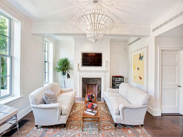 Dueling sofas in front of a marble fireplace with a long wooden coffee table between them, an area rug and a white chandelier 