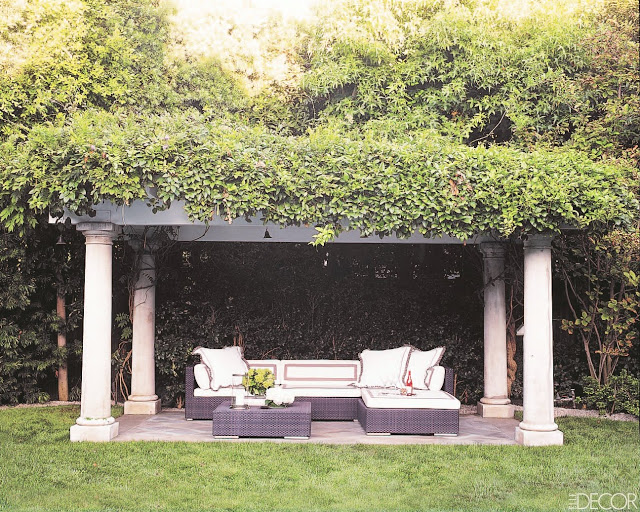 Backyard with an arbor made up of Doric columns and vines with an outdoor living room underneath