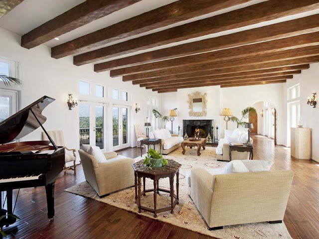 Living room with fireplace, arched doorways, wood floors, exposed wood beam ceiling, grand piano, dueling sofas with matching arm chairs and Moroccan side tables