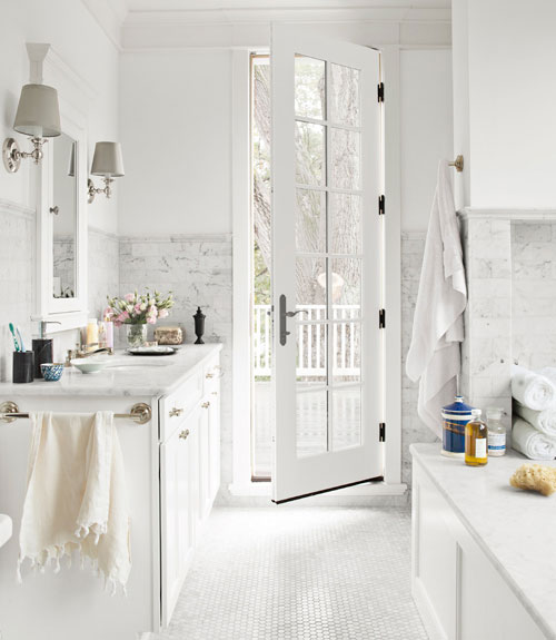 White bathroom with Carrara marble floors=in the form of a hexagon mosaic, counters and tub surround, a French door leads to a patio
