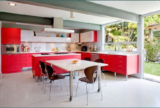 Kitchen and dining area with reed cabinets and drawers, a red island with a white counter top, white table with wood chairs and a sliding glass door that leads outside