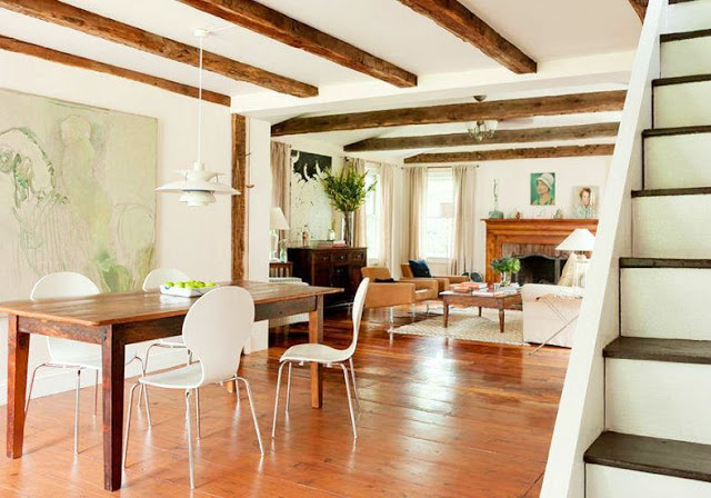 Dining room in a farmhouse with wood floor, reclaimed wood table, modern white seats, exposed beam ceiling and white pendant light