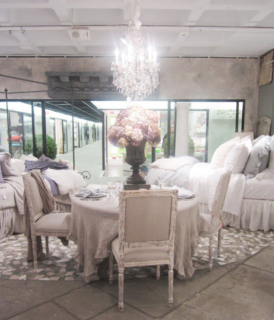 Christian Mosso Associates showroom with a round table surrounded by painted chairs, a crystal chandelier and a large goblet style vase holding a bouquet of hydrangeas
