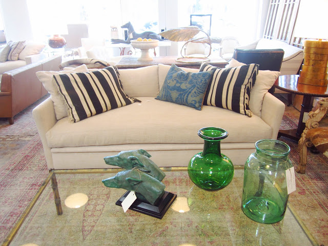 white couch with striped pillows on a vintage rug with a glass coffee table holding two green glass jars and a bust of two dogs