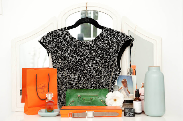Vintage beaded top hanging on a dressing table mirror with Hermes shopping bag and box, a green clutch purse, some beauty products and perfume and a photo of a little girl as accents