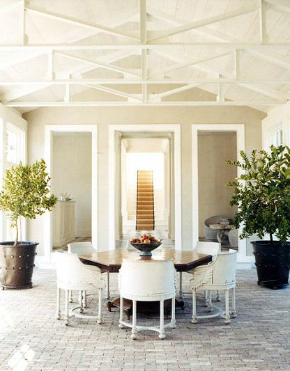 indoor dining room outdoor feel thanks to vaulted ceilings, visible beams, large metal plant pots holding small trees, octagon wood table, white wood chairs