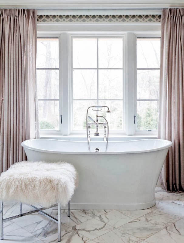 Stand alone bathtub in a girly bathroom with marble floor, floor length curtains and a furry stool