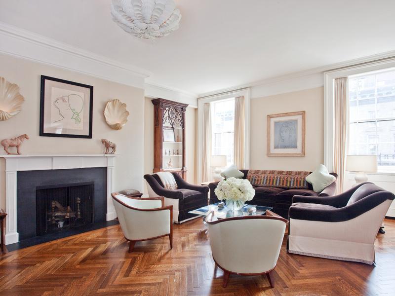 White family room in a park avenue apartment with herringbone wood floor, fireplace, white club chairs, dark purple sofa with matching armchairs and large windows with floor length curtains