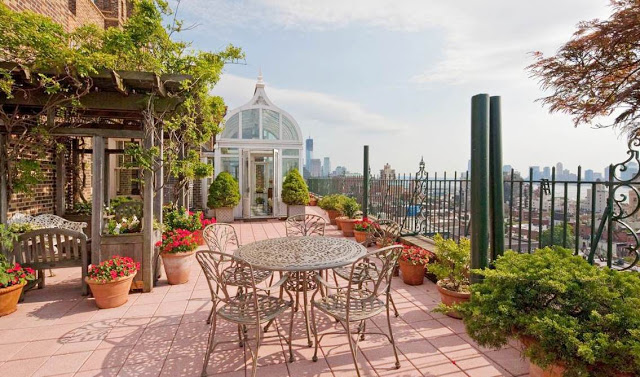 terrace with a gazebo, rows of potted plants, a metal table with matching chairs and an amazing view of New York City