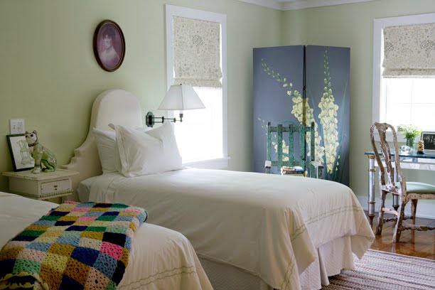 Twin bedroom with mint green walls, a wood floor, white upholstered Queen Anne style headboards, a large wardobe with a yellow flower painted on it and a vintage high back wooden chair in front of a reclaimed wood desk with a glass top