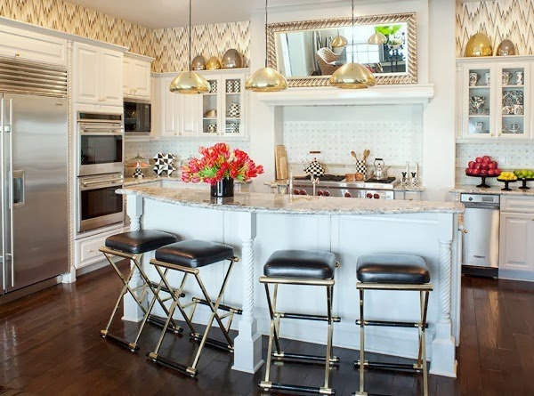 Kourtney Kardashian's kitchen with gold pendant lights, stainless appliances, silver bar stools and a white island