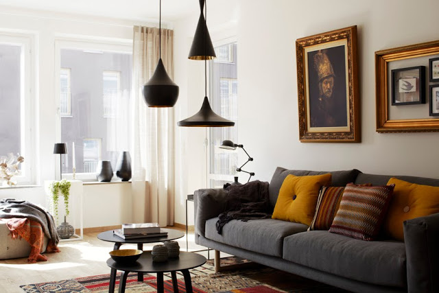 cluster of black pendant lamps over two coffee tables with a grey sofa with yellow accent pillows