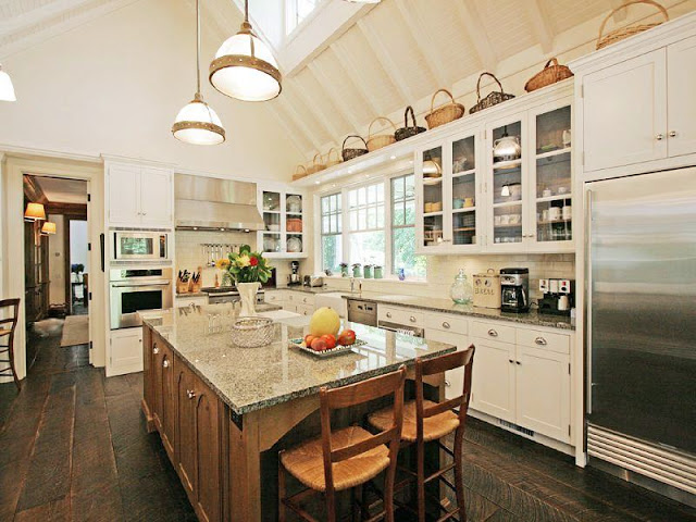 kitchen with a frame high ceiling and a skylight, rustic wood floors, white cabinets with glass upper cabinetry and an island with granite counters