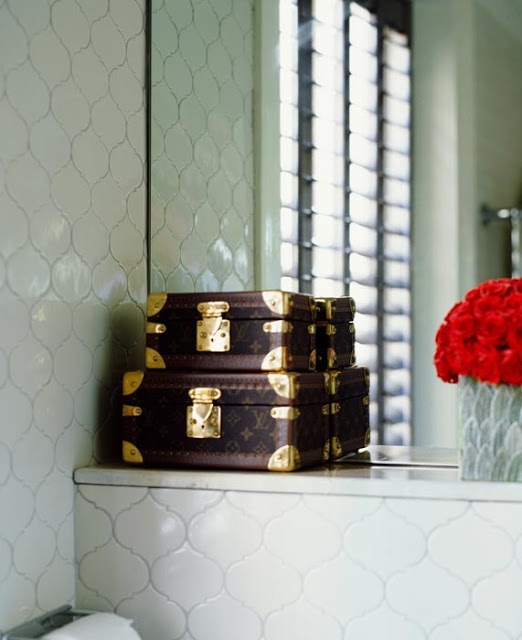 Louis Vuitton luggage being used as storage on a ledge in a tiled bath