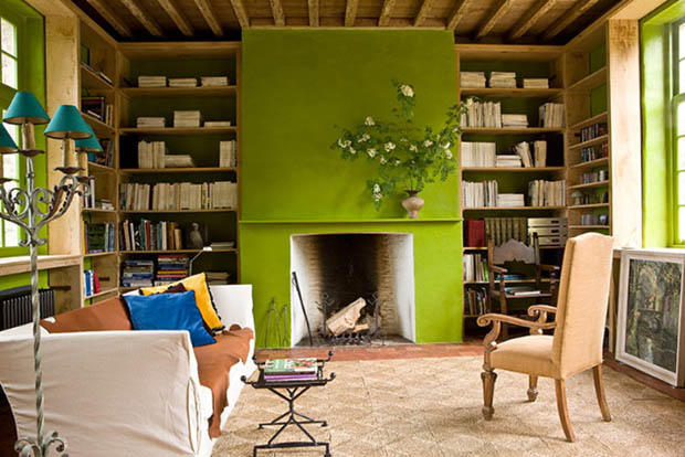 Living room with chartreuse painted fireplace, chartreuse trimmed windows, the back of the bookcases surrounding the fireplace are also painted chartreuse. The room has a white sofa, neutral area rug and wooden, and a upholstered high back chair
