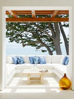 outdoor patio with white sectional sofa with blue accent pillows, light reclaimed wood coffee table and a view of the ocean
