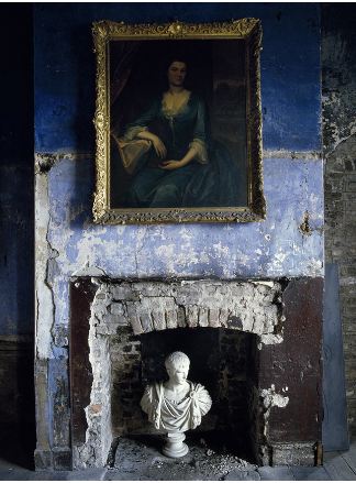 Ancient three toned fireplace with a large portrait of a woman in a gold frame and a bust inside the fireplace
