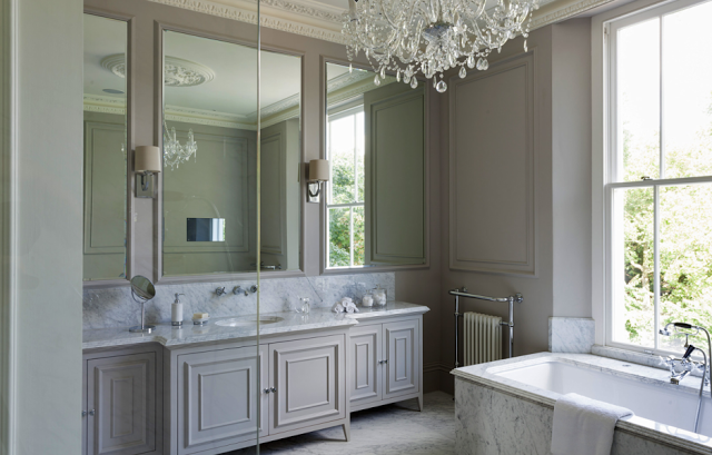 Grey master bathroom in a suburban London home with carved crown moulding, paneled walls, a crystal chandelier and marble bathtub