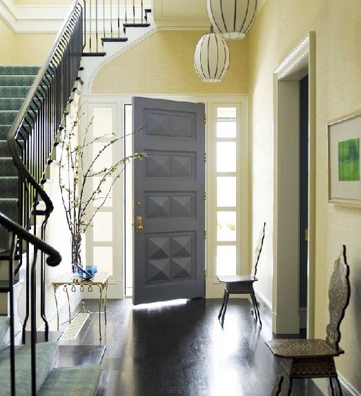 Foyer in Katie Ridder's home with pendant light, sea grass wallpaper, dark wood floor, Moroccan chairs, staircase, and a grey moulded door