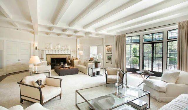 living room in a mansion with off white color scheme, large encasement windows and french doors with black trim, a fireplace and visible beams