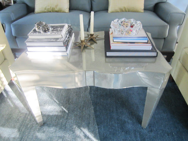 Close up of lucite coffee table with an eglomise finish and curved top, stacks of books and two candles in start shaped candleholders