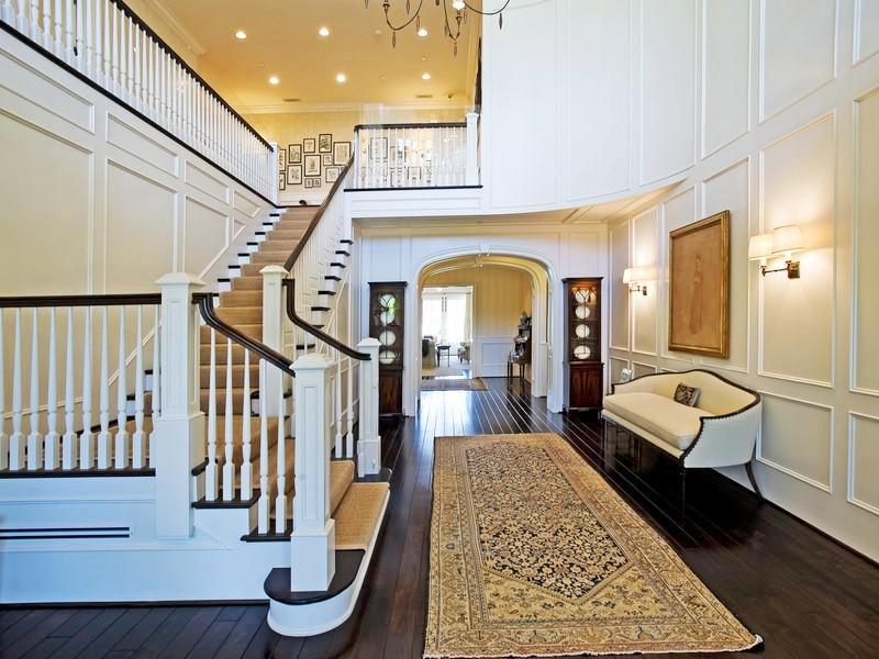 Foyer in a Pacific Palisades home with dark wood floor, paneled walls, a black and white staircase, a white Louis XIV sofa and a long Turkish rug