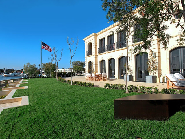 exterior of a french limestone mansion on harbor island in newport beach with a lawn, flag pole, outdoor table and deck chair