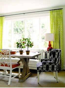 Informal dining room with a long trestle wood table, a mix of chairs and a sofa for seating, a large encasement window and floor length lime green graphic printed curtains