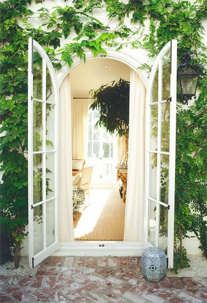 Wall covered in ivy with arched French doors leading inside propped open with a porcelain Chinese garden stooll