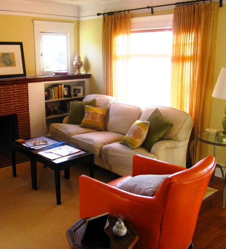 Grey sofa in a living room with green and yellow accent pillows. The living room has a sea grass rug, two black tables smushed together to function as a coffee table and an orange leather armchair