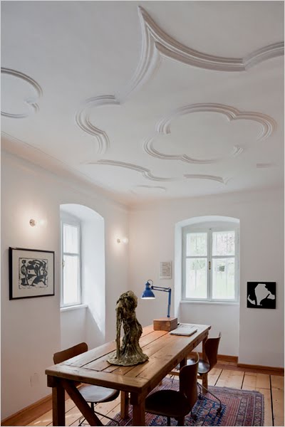 Office in the Hammerhaus castle with baroque detailing on the ceiling, a large wood table surrounded by three leather chairs, a Christina Zurfluh sculpture, knotted wood floor, and a Turkish rug