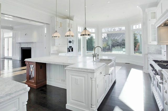 alternative view of the kitchen with hardwood floors, white marble counters, stainless steel appliances, white cabinets and a huge island with pendant lights