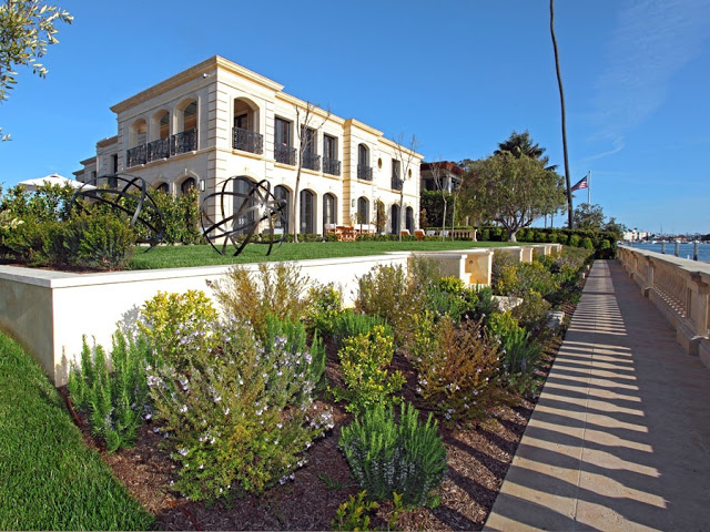Exterior of french limestone mansion on harbor island in newport beach California with a lawn, backyard, an ocean view and two round sculptures