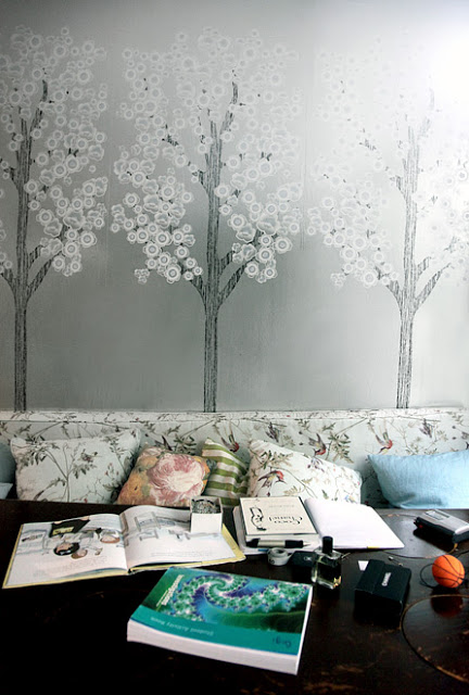 Dining area doubles as a reading space with grey wallpaper depicting trees, floral bench seating and comfy accent pillows