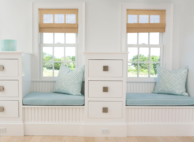 two short window seats divided by a white drawers with blue cushions and blue and white geometric print accent pillows