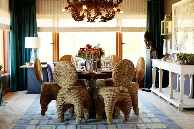 dining room with wicker chairs surroudning a wood table with a flower arrangement, a chandelier with branches covered in leaves and floor length turquoise curtains