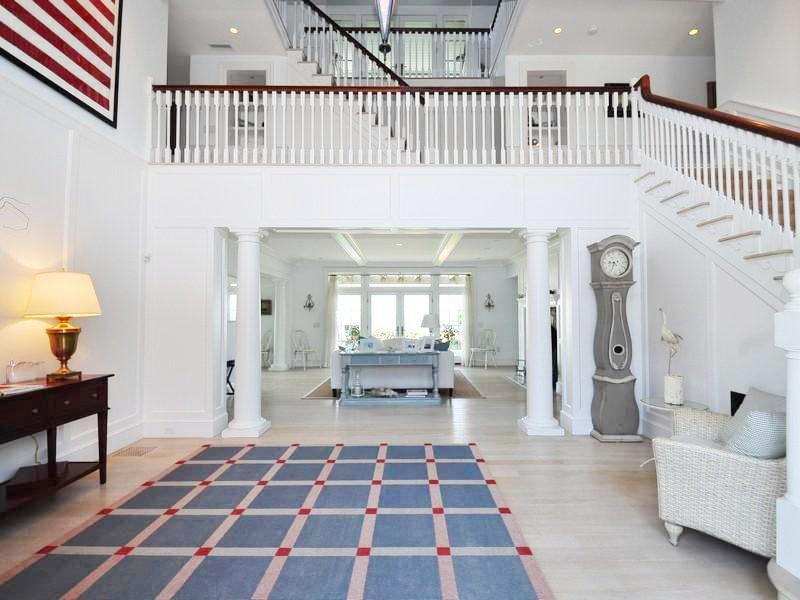Nautical theme foyer with white staircase, light wood floor, blue, white and red rug, white wicker chairs and a view of the living room