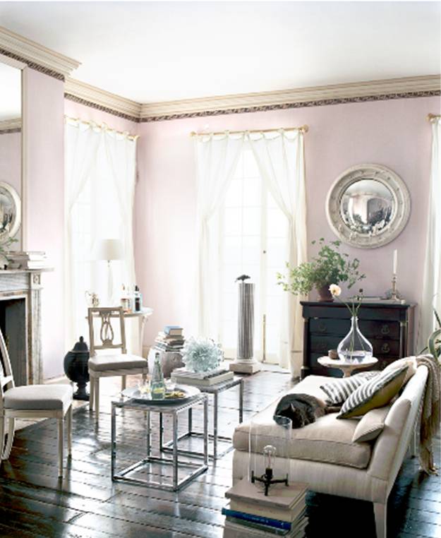 Living room with lavender walls, dark wood floor, mercury side tables, a white sofa, breeze white curtains and a round mirrors hanging above a dark wood chest of drawers