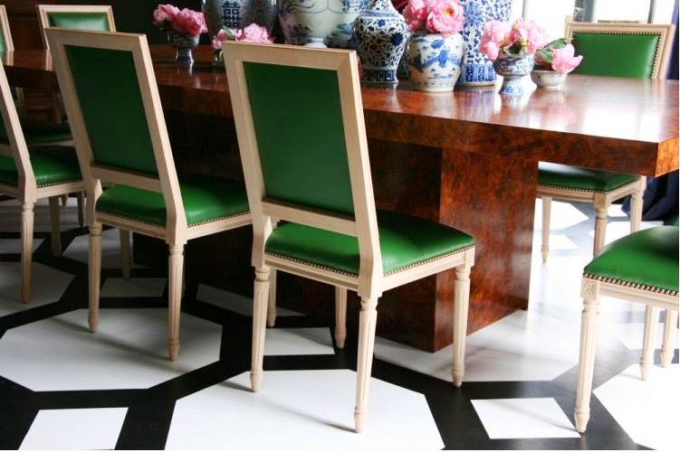 Close up of the green upholstered chairs and their nailhead trim and the black and white painted floor in a dark living room