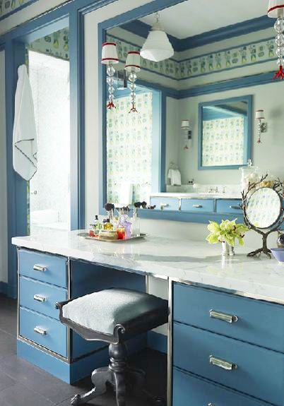 Vanity in a master bathroom with blue cabinets, marble counters, and a stool with a blue velvet cushion