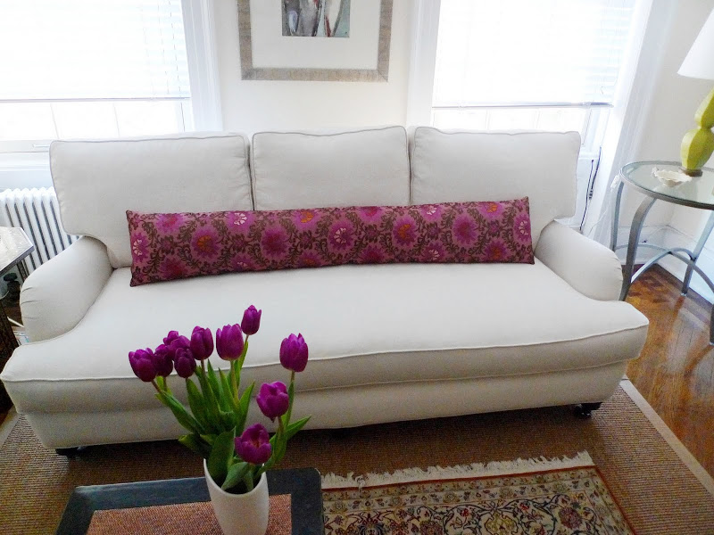 Light grey sofa in a living room with a long pink flower printed pillow on a sea grass rug