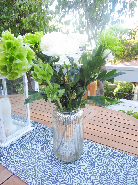 China Mums in white and some other green florals on dining table in a mercury glass hurricane lamp