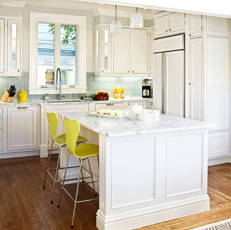 Kitchen with white cabinets and drawer, light blue backsplash, a Carrara marble countertops with a matching island. At the island are two bright yellow bar stools
