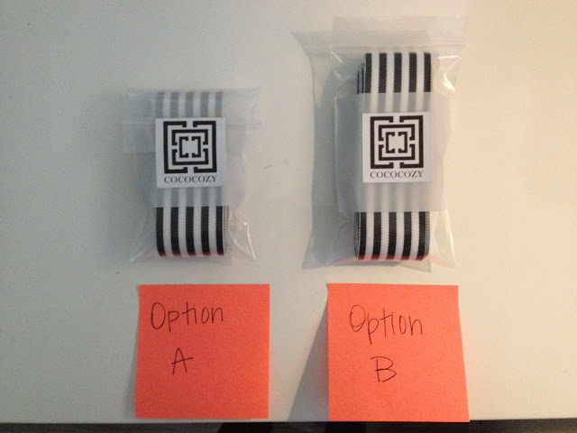 Two black and white stripped ribbons folded neatly wrapped in plastic with COCOCOZY's logos on them on a white table. An orange post it note is in front of each stack with either "Option A" or "Option B" written on it