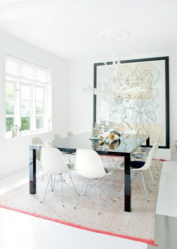 White Eames chairs in a dining room with a neutral rug with red trim and a large modern mural on the wall