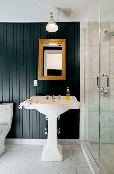 Bathroom with black beadboard walls, a pedestal sink, marble tile floor, a single pendant light and a mirror in a wood frame