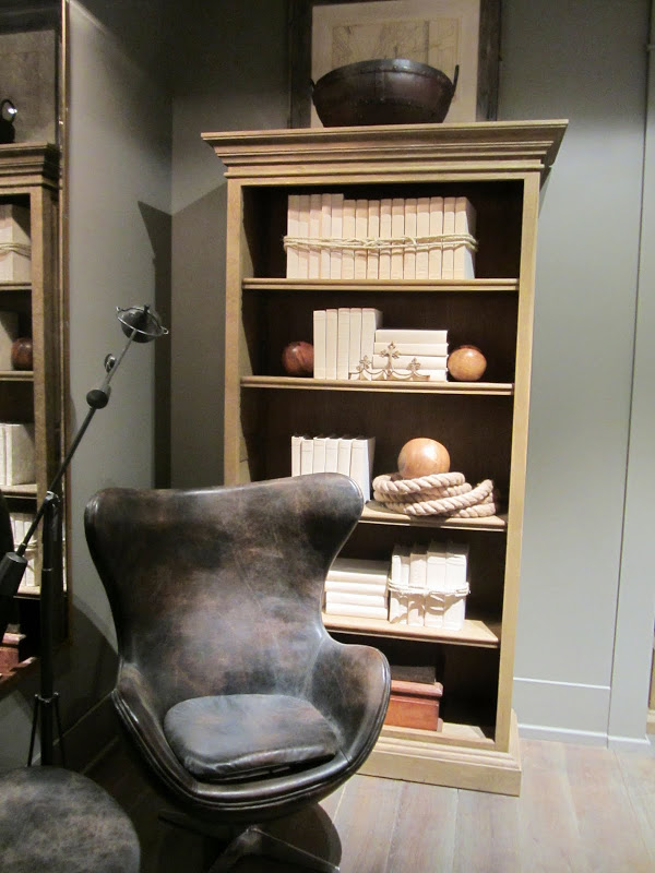 Room with grey walls and a light wood bookshelf and a modern grey leather armchair in the new Restoration Hardware