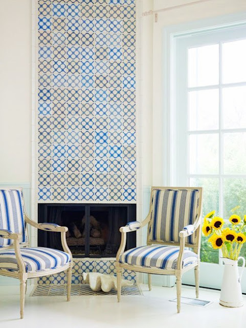Living room with fireplace covered in blue, white and yellow antique Portuguese tiles, with two upholstered blue and white striped chairs