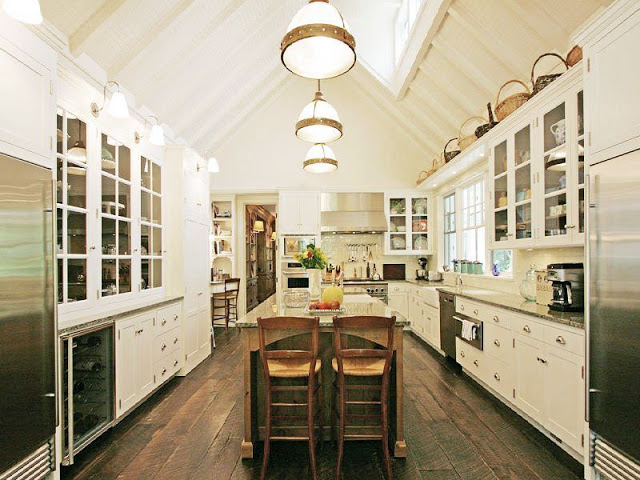 kitchen with a frame high ceiling, a skylight, rustic wood floors, white cabinets with glass upper cabinetry, a large island and stainless appliances