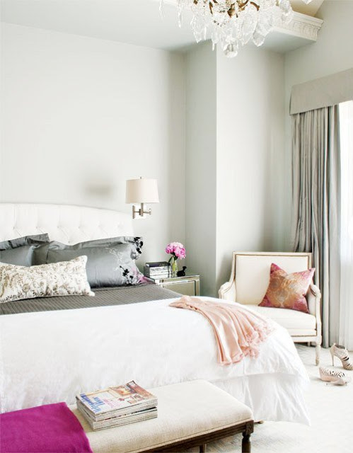 Bedroom with grey walls, an ottoman at the foot of the bed, a nightstand with a wall mounted light and an armchair